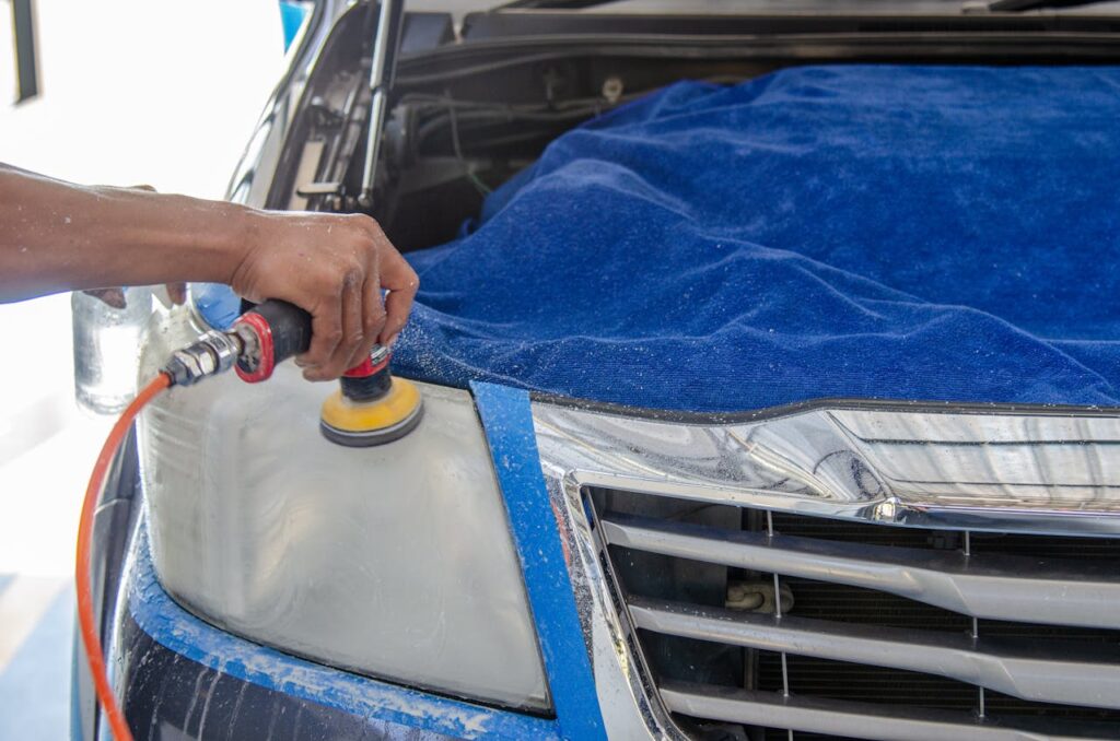 Car headlight being polished by a mechanic using an electric tool indoors.