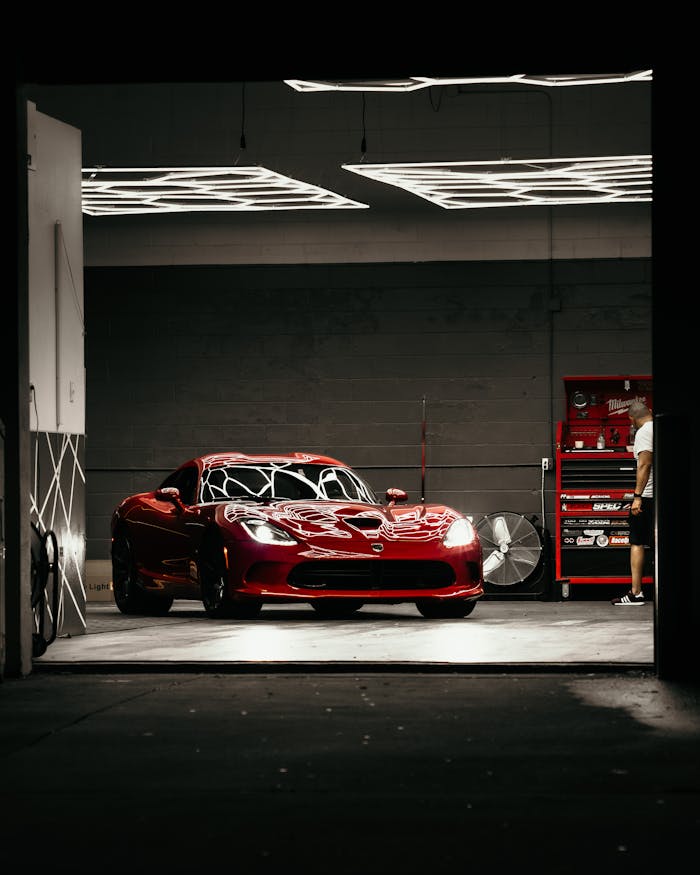 Red sports car in a garage workshop at night, showcasing detailing and elegance.